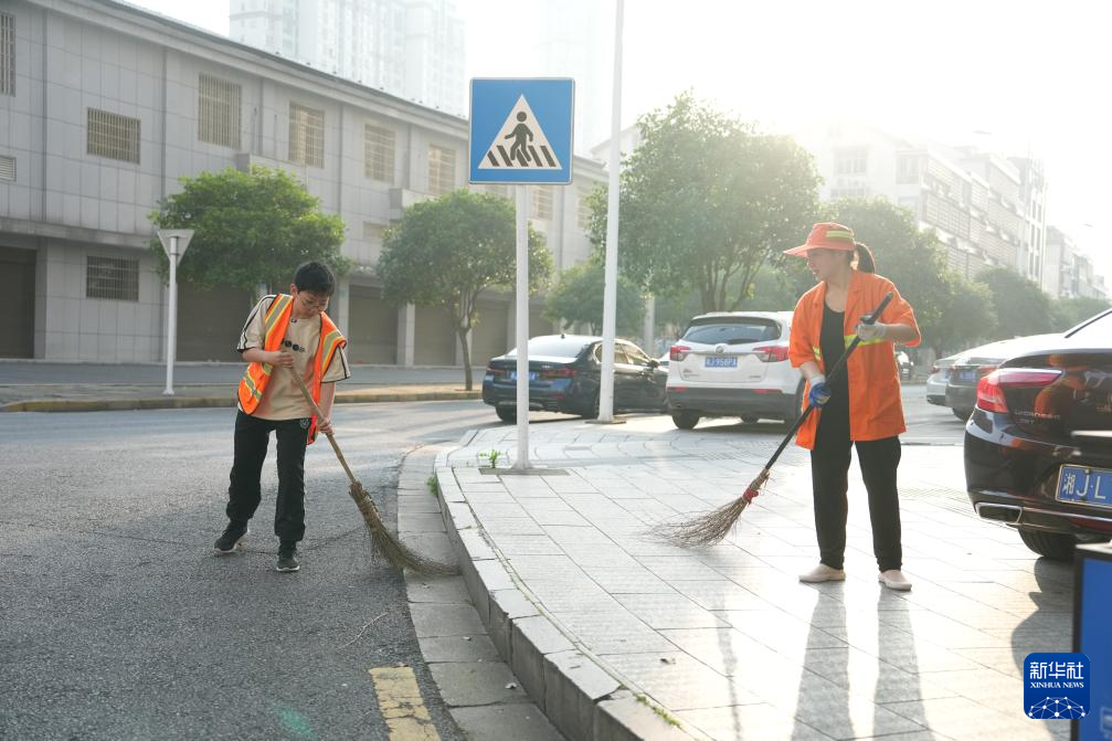 新华社记者 薛宇舸 摄5月25日,周奕唯(左)在清扫马路前帮妈妈喷防蚊药